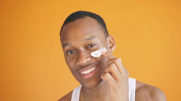 African-American Man Applies a White Mask To His Face for Healthy Glowing Skin on an Isolated Yellow