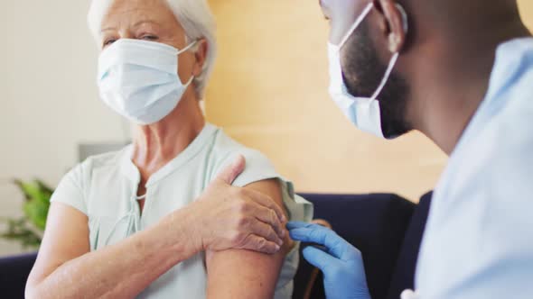 Video of african american male doctor in face mask vaccinating caucasian senior woman