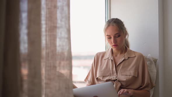 Woman Writes Report Via Computer Sitting on Sill at Home