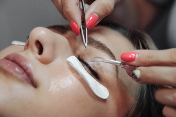 Eyelash extension process to cute young woman in beauty salon