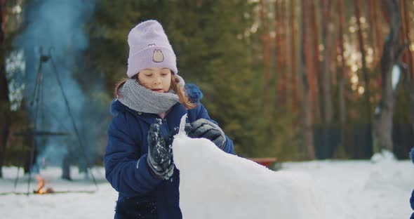 Cute Girl Builds and Plays in the Snow in the Forest