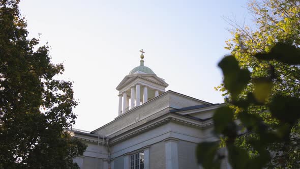 Helsinki Old Church - White pillared steeple with a golden cross catches the sun framed by nearby tr