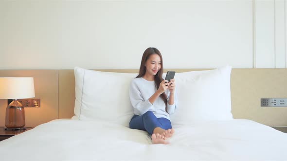 Young pretty asian woman texting on smartphone in bed, social networking concept full frame