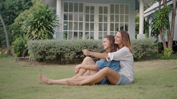 Happy Lesbian Couple Sitting on the Grass on Backyard of Their House