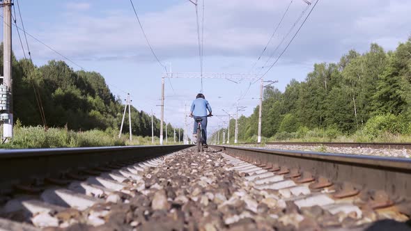 Woman Rides Away a Bicycle on Railway Sleepers in Summer Day at Countryside
