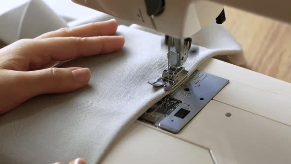 Woman hands with gray fabric sewing with a sewing machine. Women's hands sew on a sewing machine.