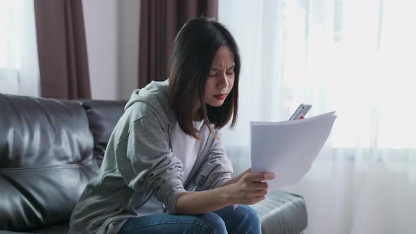 Woman holding the bill and smartphone in the living room and stressed by excessive expenses