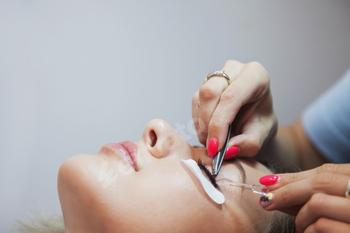 Eyelash extension process to cute young woman in beauty salon