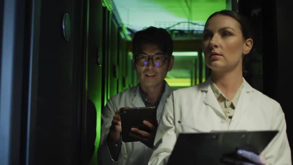 Diverse female and male it technicians in lab coats using tablet and laptop checking computer server