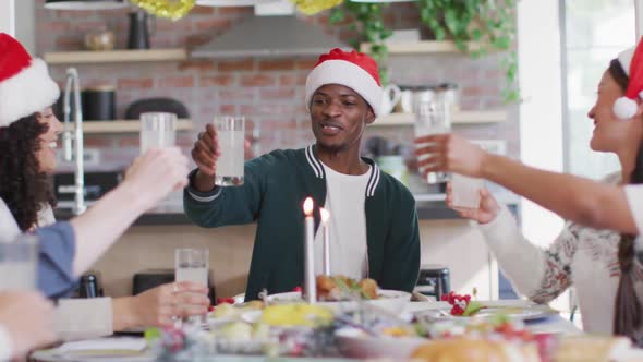 Happy group of diverse friends in santa hats celebrating meal, toasting with juice at christmas time