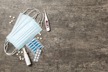 Protective face masks or surgical masks, medicine pills and thermometer on table background