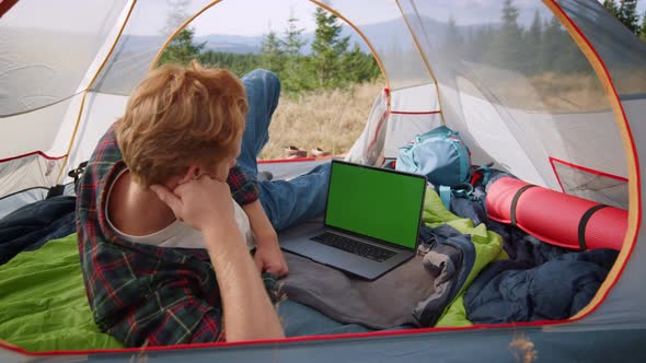 Serious Guy Watching Film on Laptop Computer with Green Screen in Tent