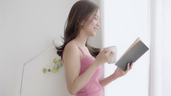 Beautiful young asian woman relax and leisure standing learning with reading book and drink coffee.