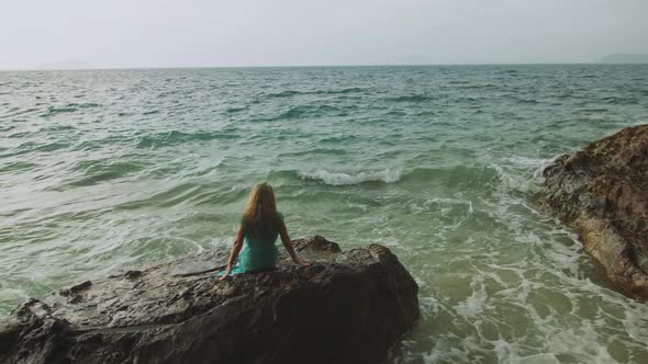 Woman Meditates Relaxes on a Rock Reef Hill in Stormy Morning Rain Cloudy Sea