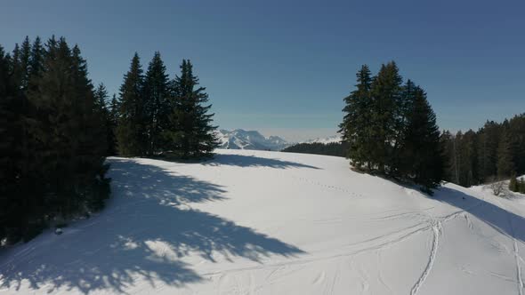 Drone flying over snow covered hill and revealing a stunning valley with green forest