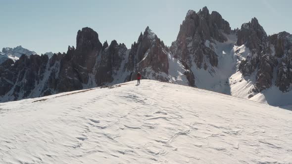 Tight circling drone shot of hiker standing on a snowy ridge overlooking the Candini group mountains