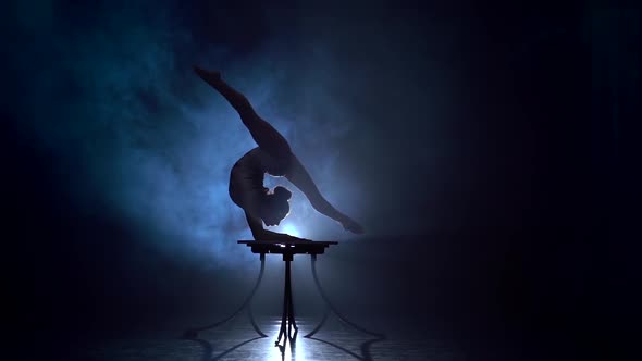 Girl Acrobat on the Table Shows the Tricks of Standing on Her Hands . Smoke Background. Slow Motion