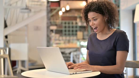 Young African Woman Celebrating Success on Laptop in Cafe