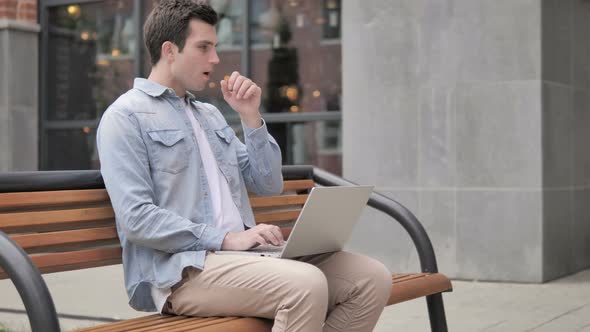 Young Man Coughing while Working on Laptop Outdoor