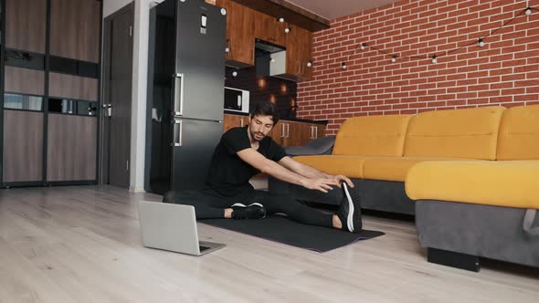 Guy Watching Flexibility Online Training on Laptop Sitting on Yoga Mat
