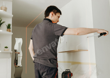 A young man checks the levelness of a shelf with a laser level.