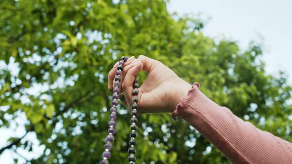 Hand of Young Believing Woman Prays in Nature and Uses Craft Rosary Beads To Count Prayer and alt