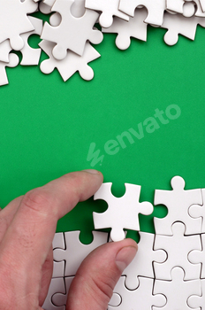 The hand folds a white jigsaw puzzle and a pile of uncombed puzzle pieces