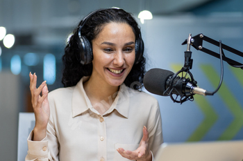 Female podcaster wearing headphones recording podcast episode in studio