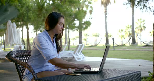 Pretty Woman Is Working with Laptop in Garden Area, Turning To Camera and Smiling Sweetly