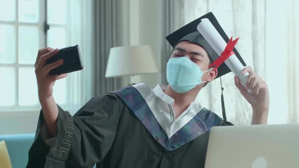 Asian Man Wearing Protection Face Mask, Taking A Selfie While Wearing A Graduation Gown And Cap