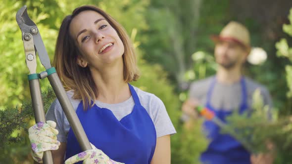 Portrait of Attractive Caucasian Woman Showing Thumb Up Holding Big Garden Cutter in the Foreground