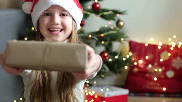 Cute Little Girl Smiling Giving Handmade Stylish Simple Christmas Gift Box in Craft Paper at Home