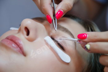 Eyelash extension process to cute pretty young woman in beauty salon