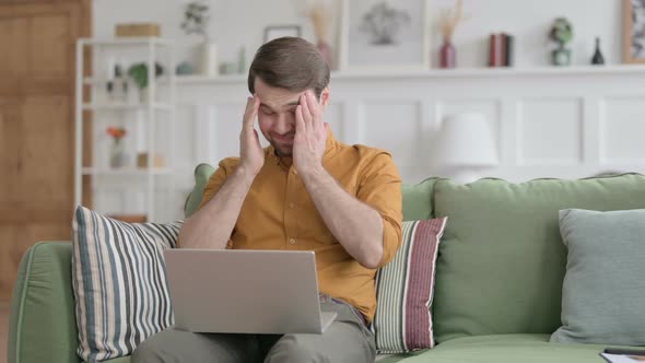 Young Man with Laptop having Headache on Sofa