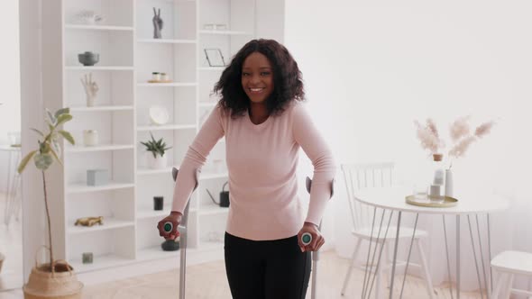 Cheerful Black Woman Standing With Crutches Posing At Home