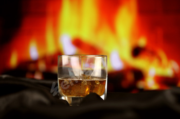 Whisky or whiskey or bourbon with ice on wooden surface on fireplace background