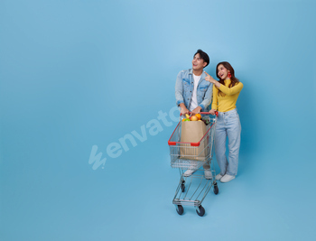 Happy Asian couple pushing shopping cart pointing finger promotion at the supermarket