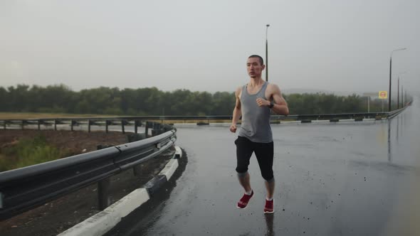 Asian Man of Athletic Build Runs Marathon on Highway During Rain Front View