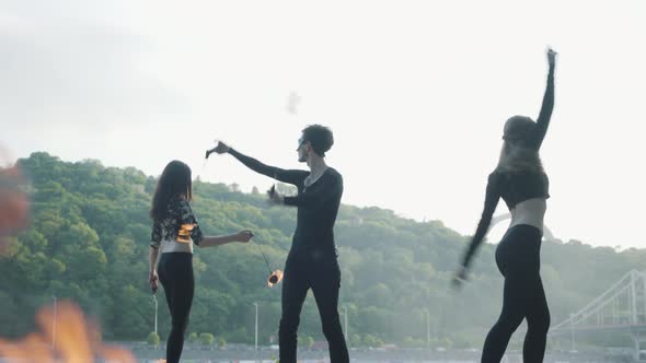 Young Slim Man and Two Beautiful Women Simultaneously Perform Show with Flame