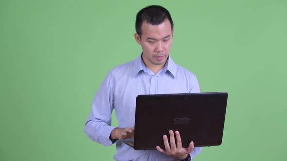 Happy Asian Businessman Talking While Using Laptop