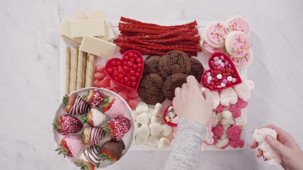 Flat lay. Step by step. Arranging cheese board with candies and cookies for Valentines Day.