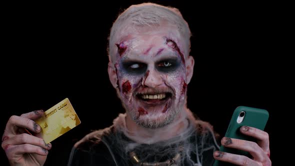 Sinister Man Halloween Zombie Using Credit Bank Card and Smartphone While Purchases Online Shopping