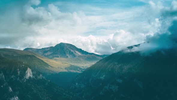 A mountain with a snowfield and a gorge covered with a forest amidst clouds and fog