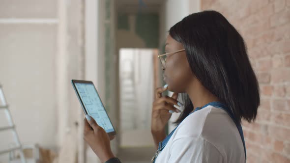 Young Attractive Afro Woman Watching Apartment Blueprint on Smartphone During Renovation