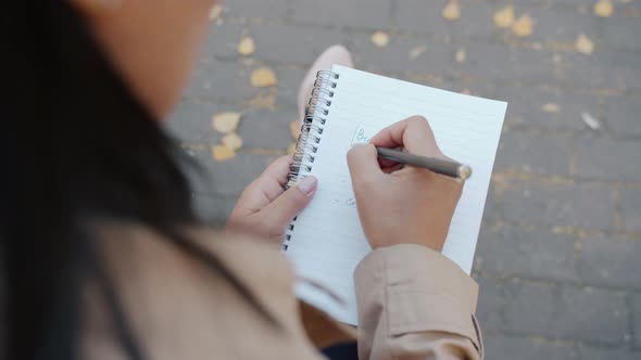 Closeup of Female Hand Writing in Notebook While Young Entrepreneur Planning Startup Business