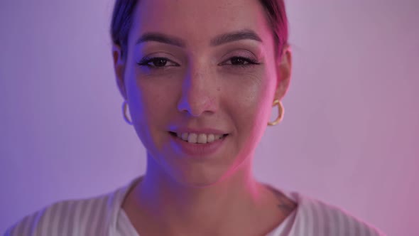 Slow Motion Close Up Of Gorgeous Young Woman Looking At Camera and Smiling Under Blue And Purple