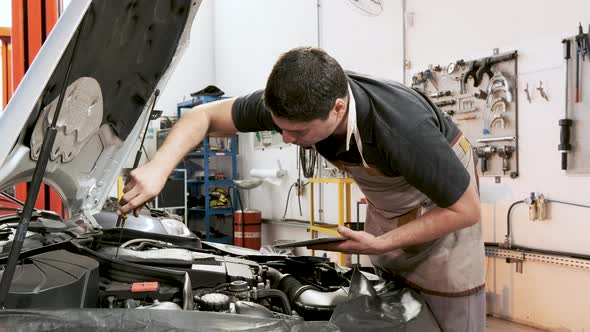 Hispanic male car mechanic holding clipboard reinserts dipstick