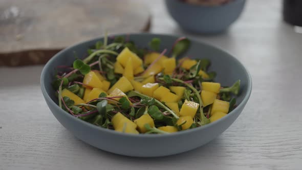 Man Put Mozzarella Balls in Salad with Micro Greens in Blue Bowl