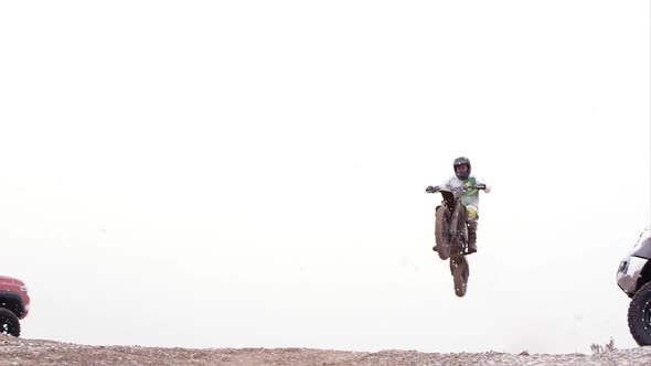 Motocross rider jumping over hill between two SUVs.