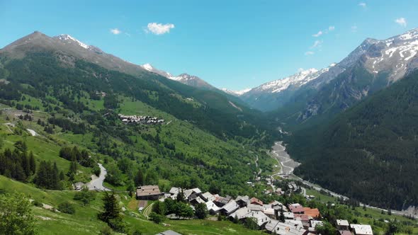 Aerial: flying over alpine valley, scenic forest snowcapped mountain range and winding road